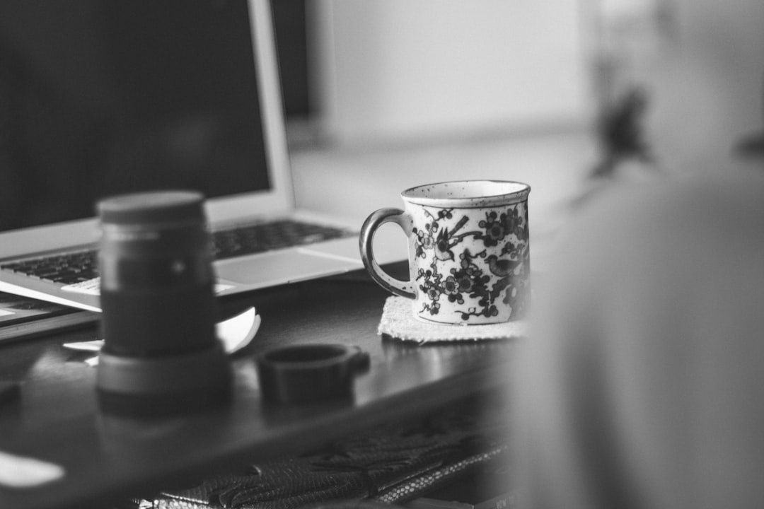 Laptop, kaffekopp och burk på ett skrivbord i svartvitt